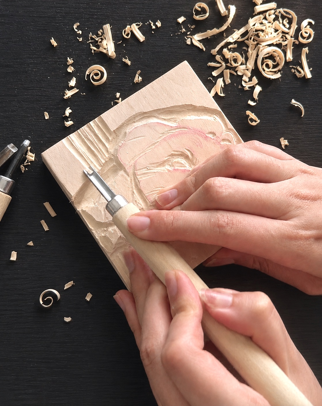 Hands carving a wooden pet portrait, surrounded by wood shavings